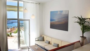 A modern living room with a sofa, a table, and a large window with a view of a marina and boats.