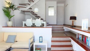 A modern living room with a sofa, a coffee table, and a staircase leading to a dining area with chairs and a table.