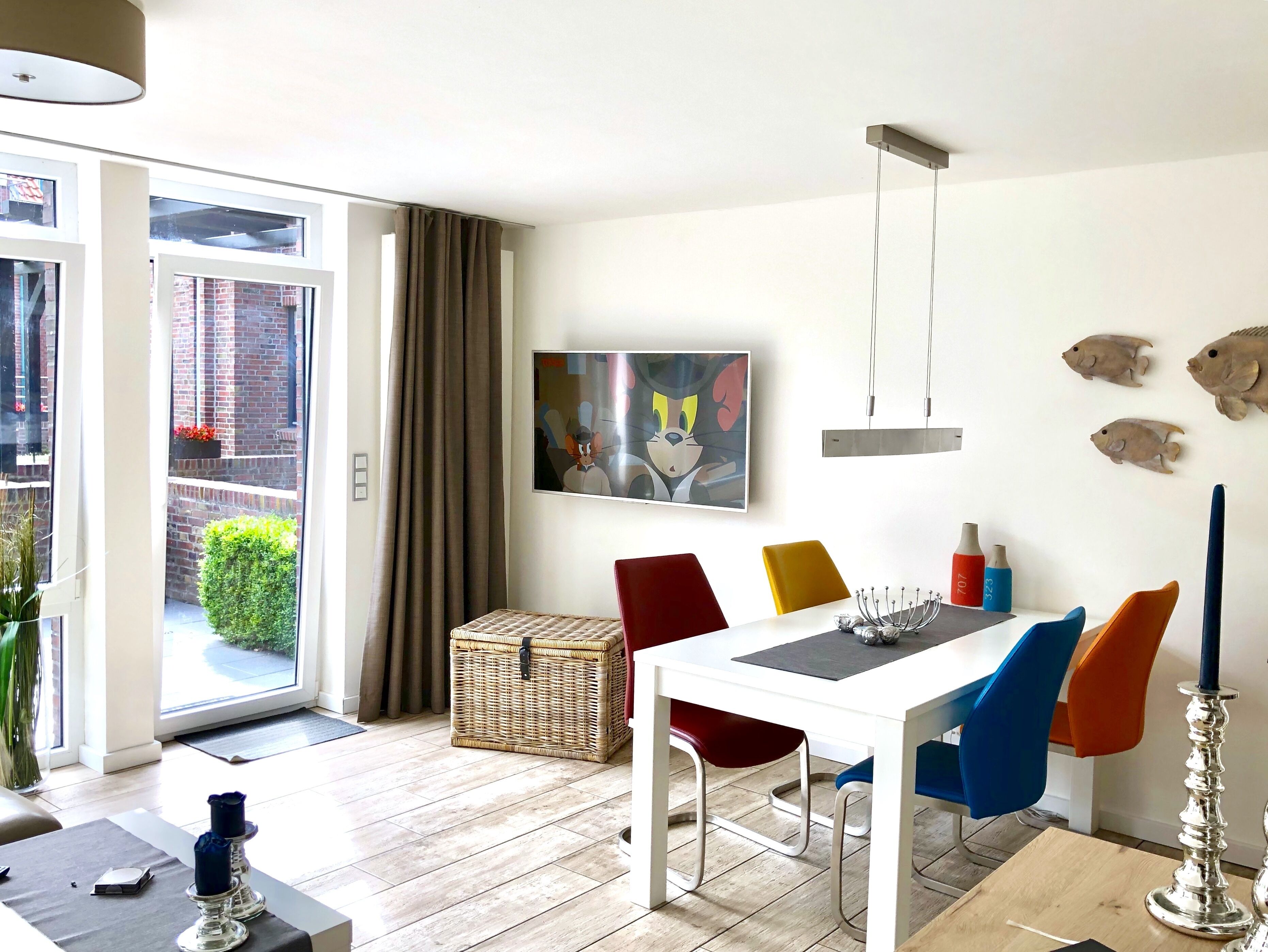 Un'area pranzo con tavolo bianco, sedie colorate, un lampadario e un'ornamento a forma di pesce appeso al muro.