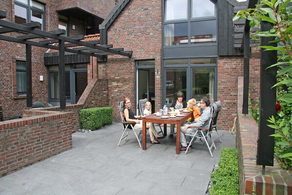An outdoor patio with a brick building, a table with chairs, and a small garden area.