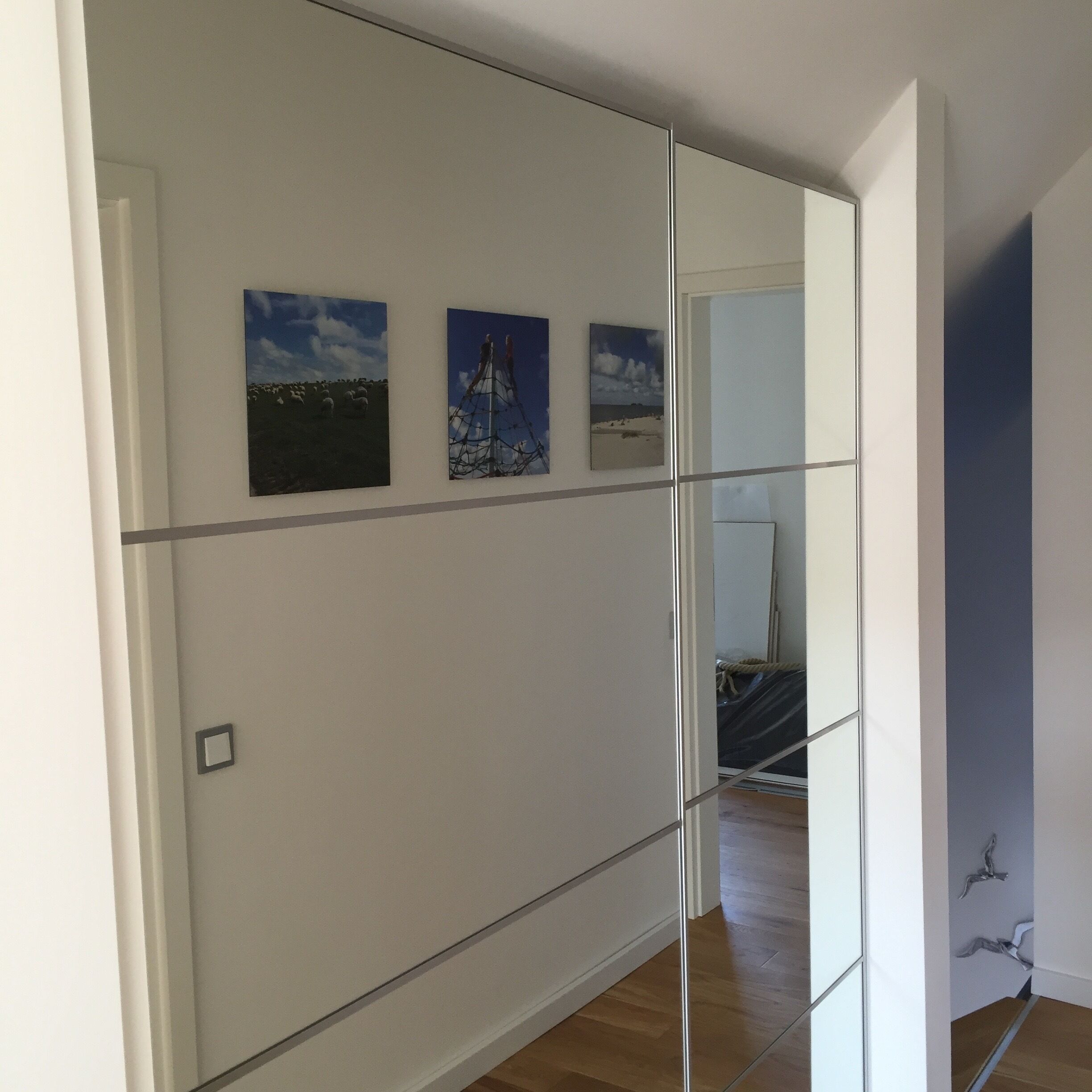 A room with a large mirror reflecting a beach scene, a bed, and a door.