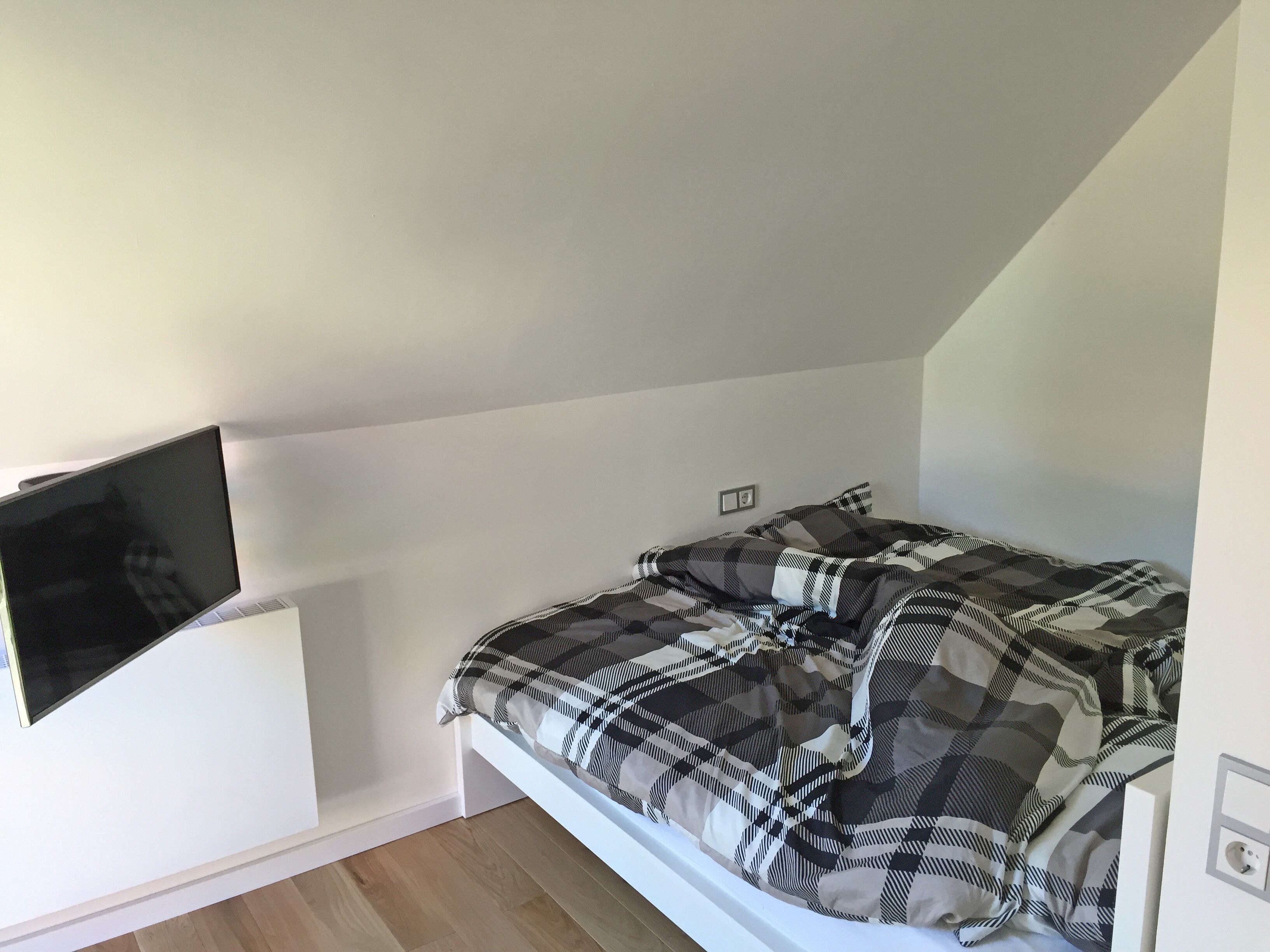 A bedroom with a bed, a mounted TV, and a power outlet on the wall.