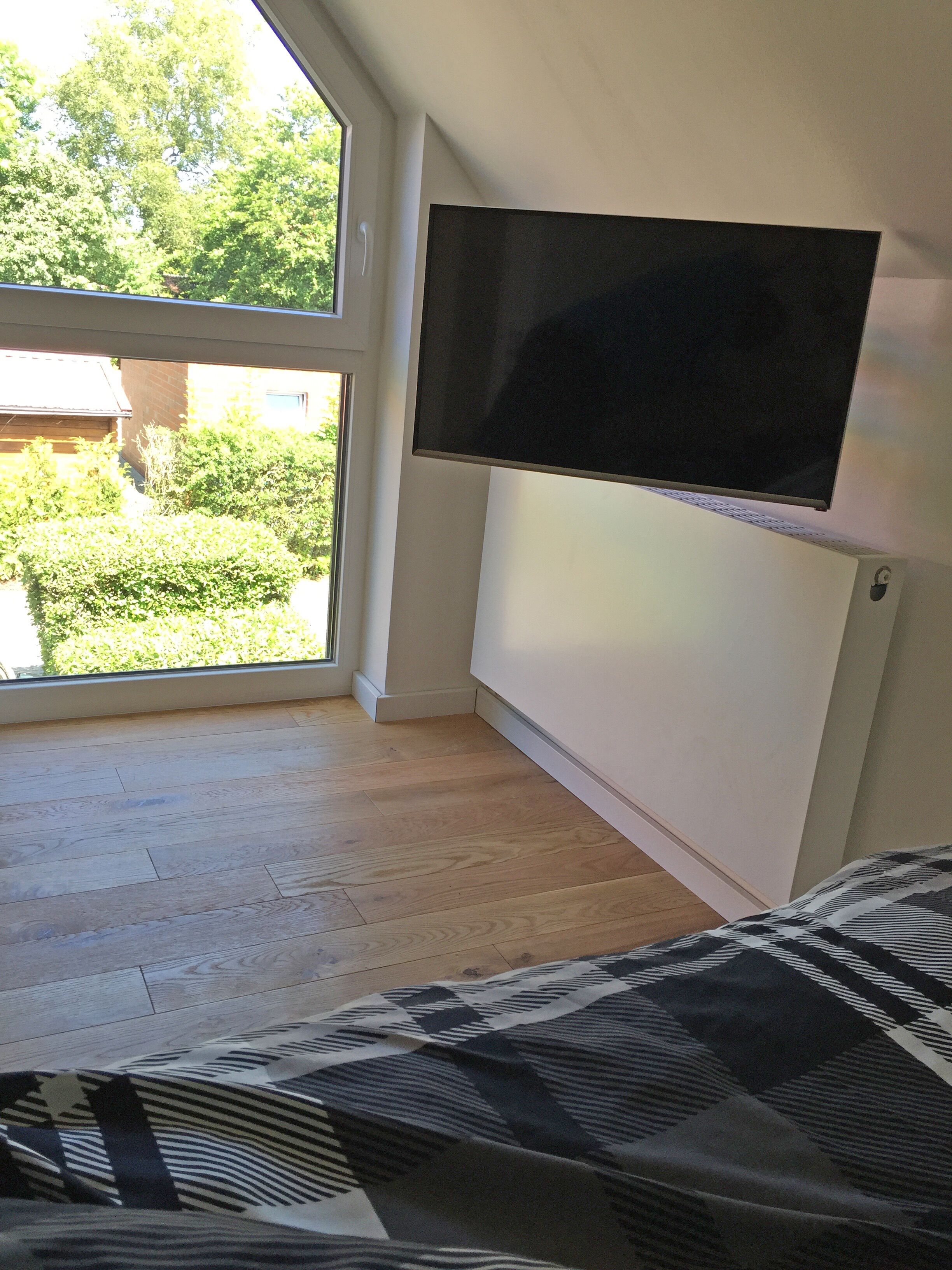 Una habitación con un ventanal amplio, un televisor montado y una colcha con estampado.