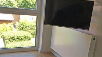 Una habitación con un ventanal amplio, un televisor montado y una colcha con estampado.