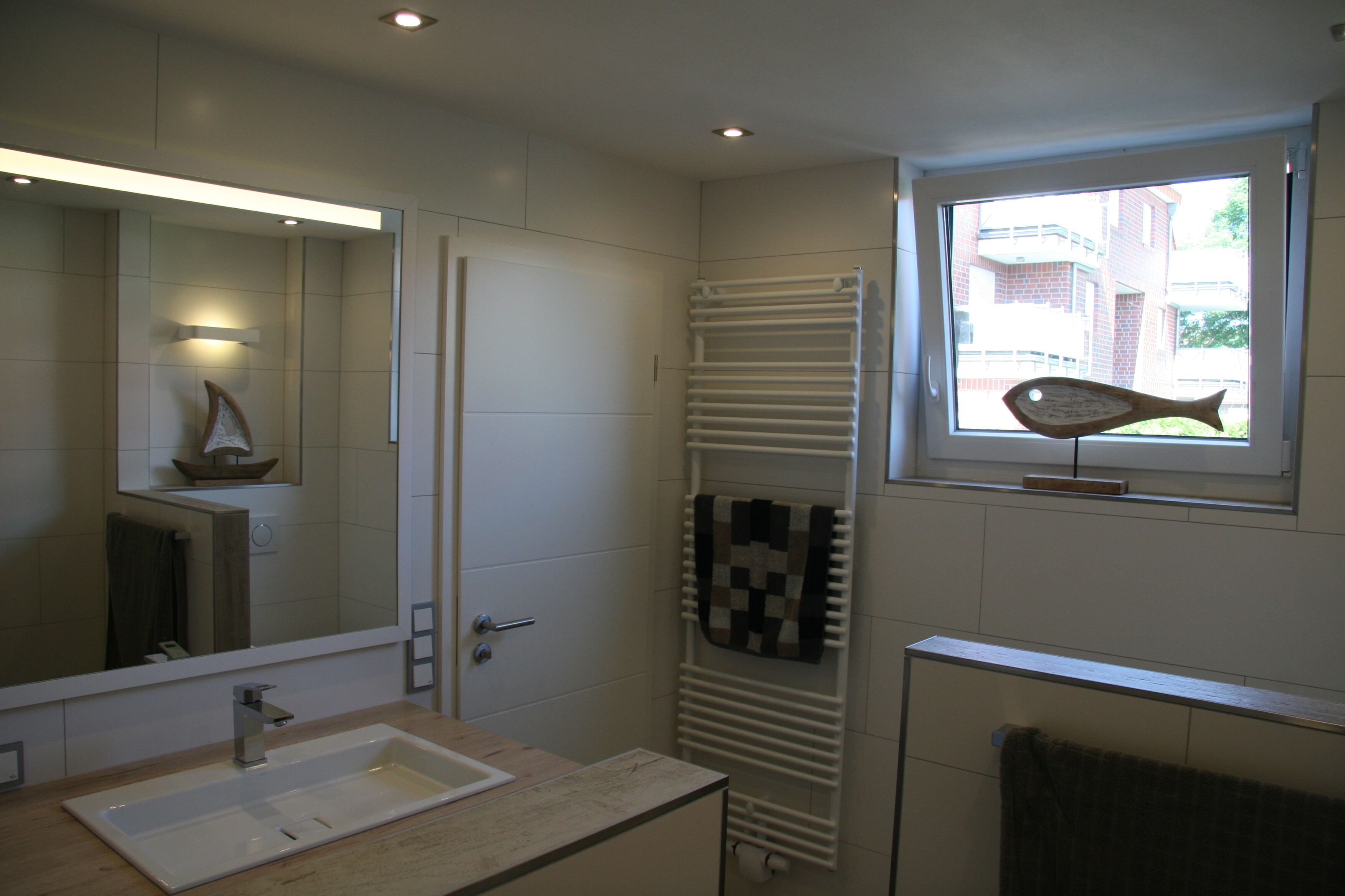 Une salle de bain équipée d’un lavabo, d’un miroir, d’un porte-serviettes et d’une fenêtre donnant sur des immeubles.