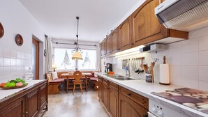 A kitchen with wooden cabinets, a dining table with chairs, a built-in oven, and a window with a view of trees. - Apartment on the Zugspitze (Grainau)