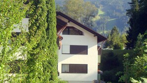 A two-story house with a sloped roof, surrounded by lush greenery and a well-maintained lawn. - Apartment on the Zugspitze (Grainau)