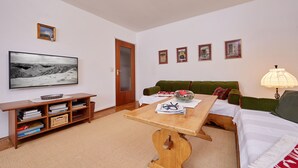 A living room with a wooden coffee table, a green sofa, a television mounted on the wall, and a door leading to another room. - Apartment on the Zugspitze (Grainau)