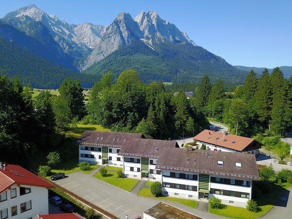 A modern building with a red roof, surrounded by lush greenery and mountains in the background. - Apartment on the Zugspitze (Grainau)
