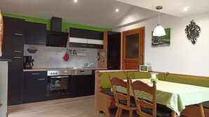 A compact kitchen with modern appliances, a dining area with wooden chairs, and a green wall. - Vacation on the farm in beautiful Koesslarn in Lower Bavaria (Kößlarn)