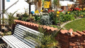 A traditional chalet with a wooden balcony, a stone wall, and a variety of potted plants and flowers. - Vacation on the farm in beautiful Koesslarn in Lower Bavaria (Kößlarn)