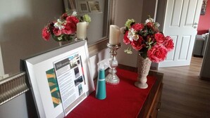 Un mostrador de recepción con un cartel de bienvenida enmarco, un atomizador azul turquesa y dos jarrones con flores rojas.