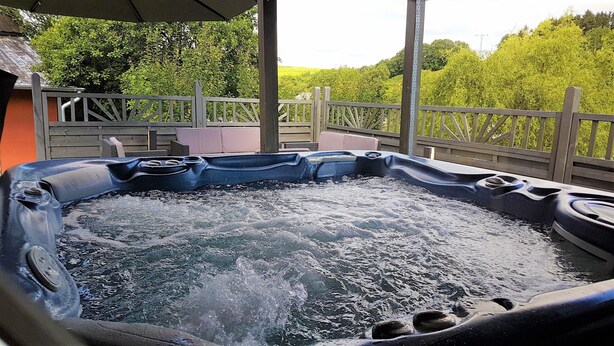 A hot tub with a wooden deck and a view of lush greenery. - Holiday home for sole use, garden sauna, outdoor whirlpool, WLAN, play barn (Plütscheid)