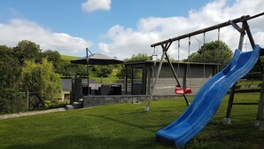 A playground with a blue slide and swings, surrounded by a grassy area and trees. - Holiday home for sole use, garden sauna, outdoor whirlpool, WLAN, play barn (Plütscheid)
