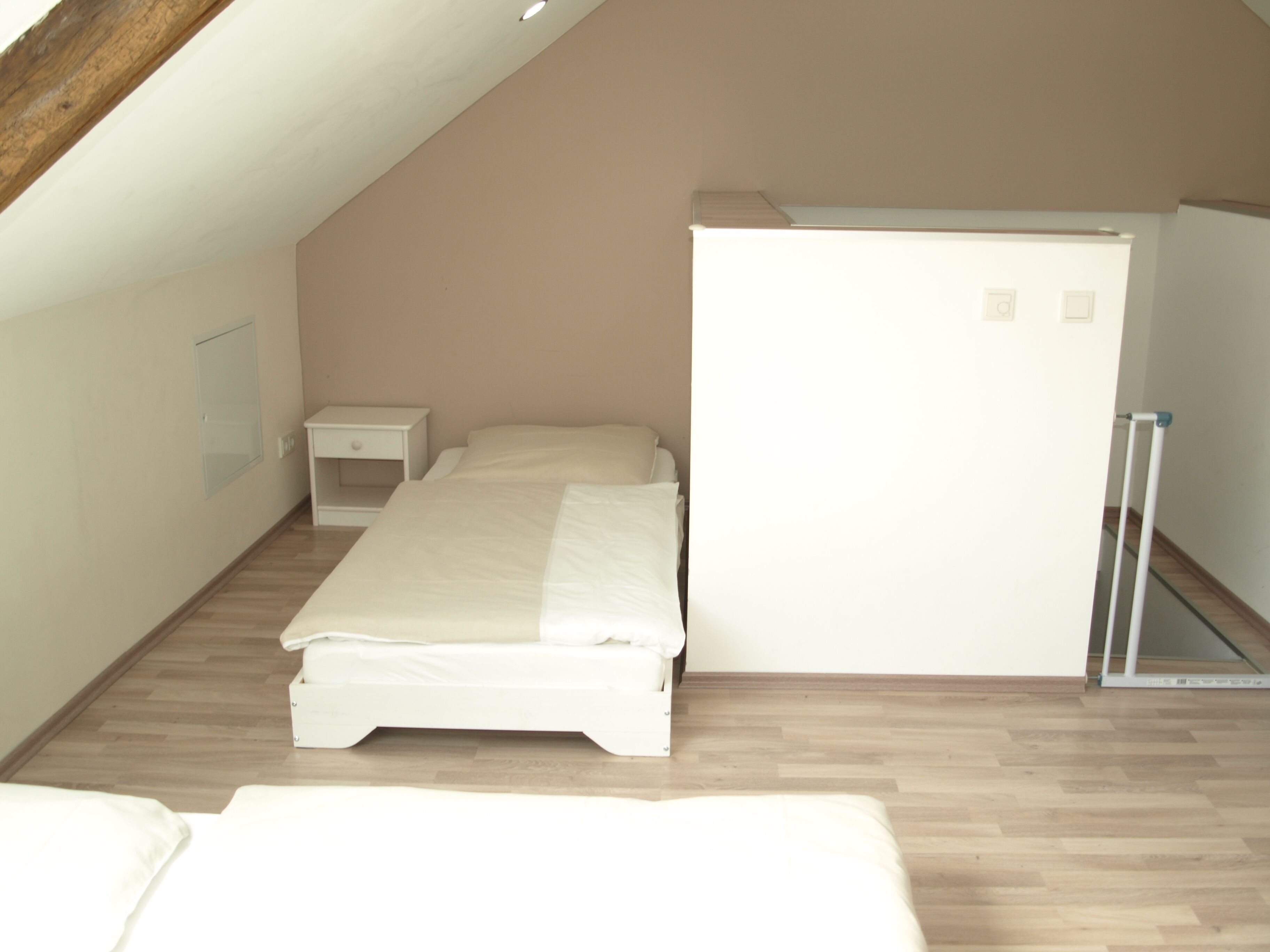 A small, white, single-bed room with a wooden floor, a white wardrobe, and a small bedside table.
