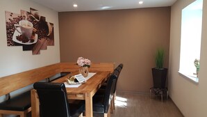 A dining area with a wooden table, black chairs, a vase with flowers, and a wall with a coffee-themed artwork. - Holiday home for sole use, garden sauna, outdoor whirlpool, WLAN, play barn (Plütscheid)