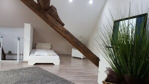 A modern bedroom with a sloped ceiling, a wooden beam, a bed, a nightstand, a potted plant, and a view of the outdoors. - Holiday home for sole use, garden sauna, outdoor whirlpool, WLAN, play barn (Plütscheid)