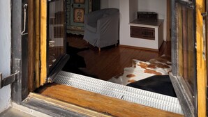 A room with a wooden floor, a bed covered with a grey blanket, a wooden cabinet with decorative panels, and a clock on the wall.