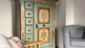 A room with a vintage teal cabinet with floral designs, a grey sofa, and a patterned throw pillow.