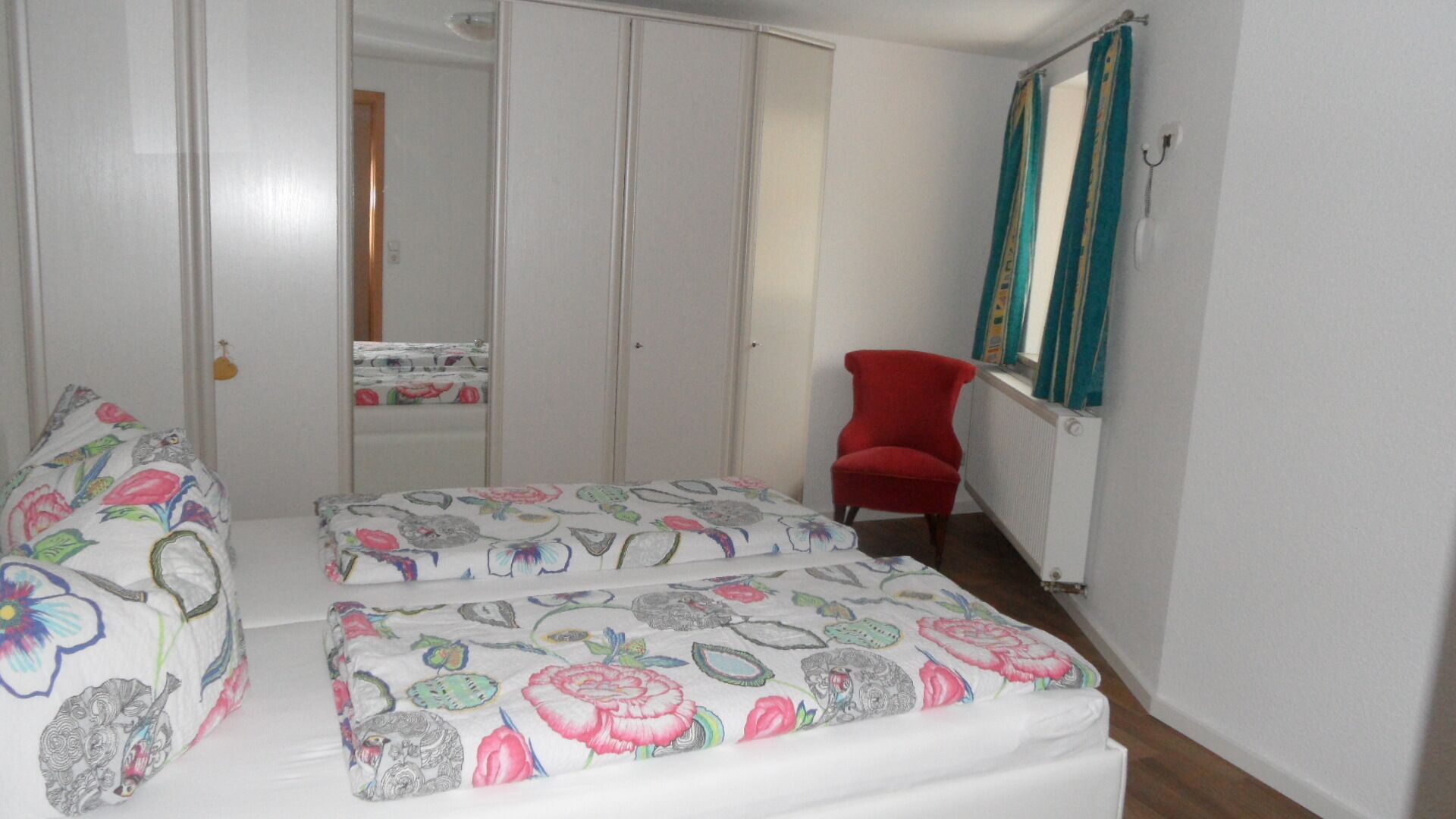 A bedroom with a bed, a chair, a wardrobe, and a mirror.