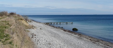 A pebbly beach with a wooden pier extending into calm waters.