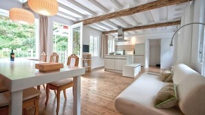 Ein großzügiger Wohnbereich mit Holzboden, einem weißen Sofa, einem Esstisch mit Stühlen und Pendelleuchten.