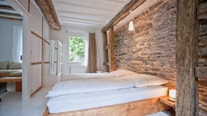 Ein Schlafzimmer mit einem hölzernen Bett, einer Steinwand und Blick auf Grünfläche.