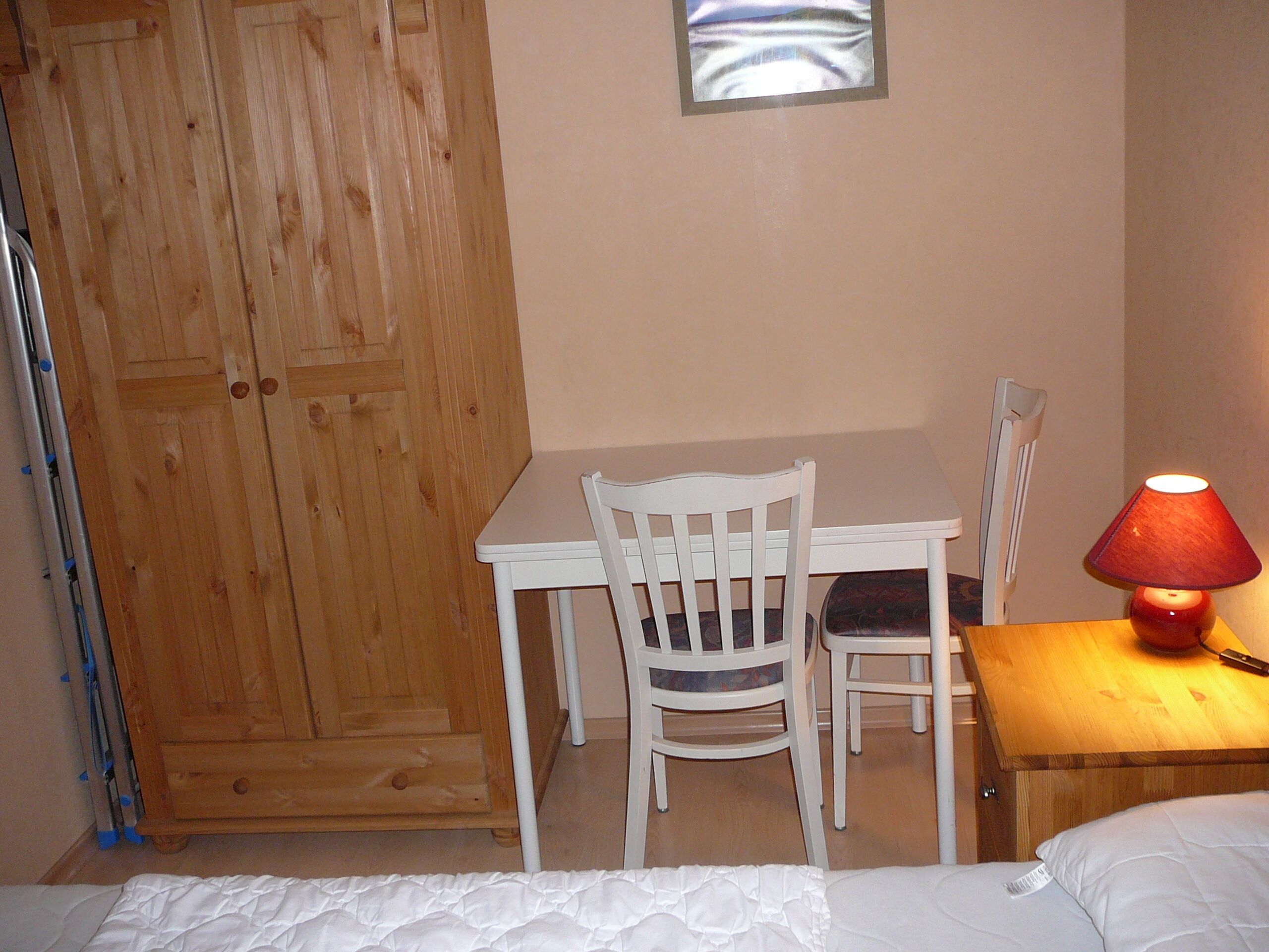 Una habitación pequeña con un escritorio de madera, una silla blanca, una cama y una lámpara roja.