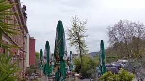 An outdoor seating area with tables and chairs, surrounded by green umbrellas, and a view of parked cars and buildings in the background. - HAARDTER WINZER (Whg. 4) renovated and lovingly decorated "Pfalzcard-Partner" (Neustadt an der Weinstraße)