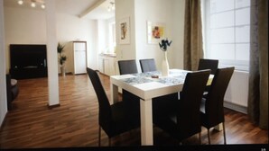 A modern dining area with a white table and black chairs, a small vase with flowers, and a window with curtains. - HAARDTER WINZER (Whg. 4) renovated and lovingly decorated "Pfalzcard-Partner" (Neustadt an der Weinstraße)