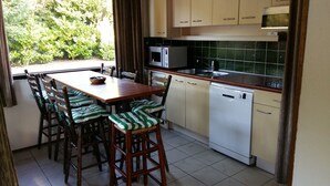 Zona pranzo con tavolo e sedie in legno, forno a microonde, lavastoviglie e finestra vista su spazi verdi.