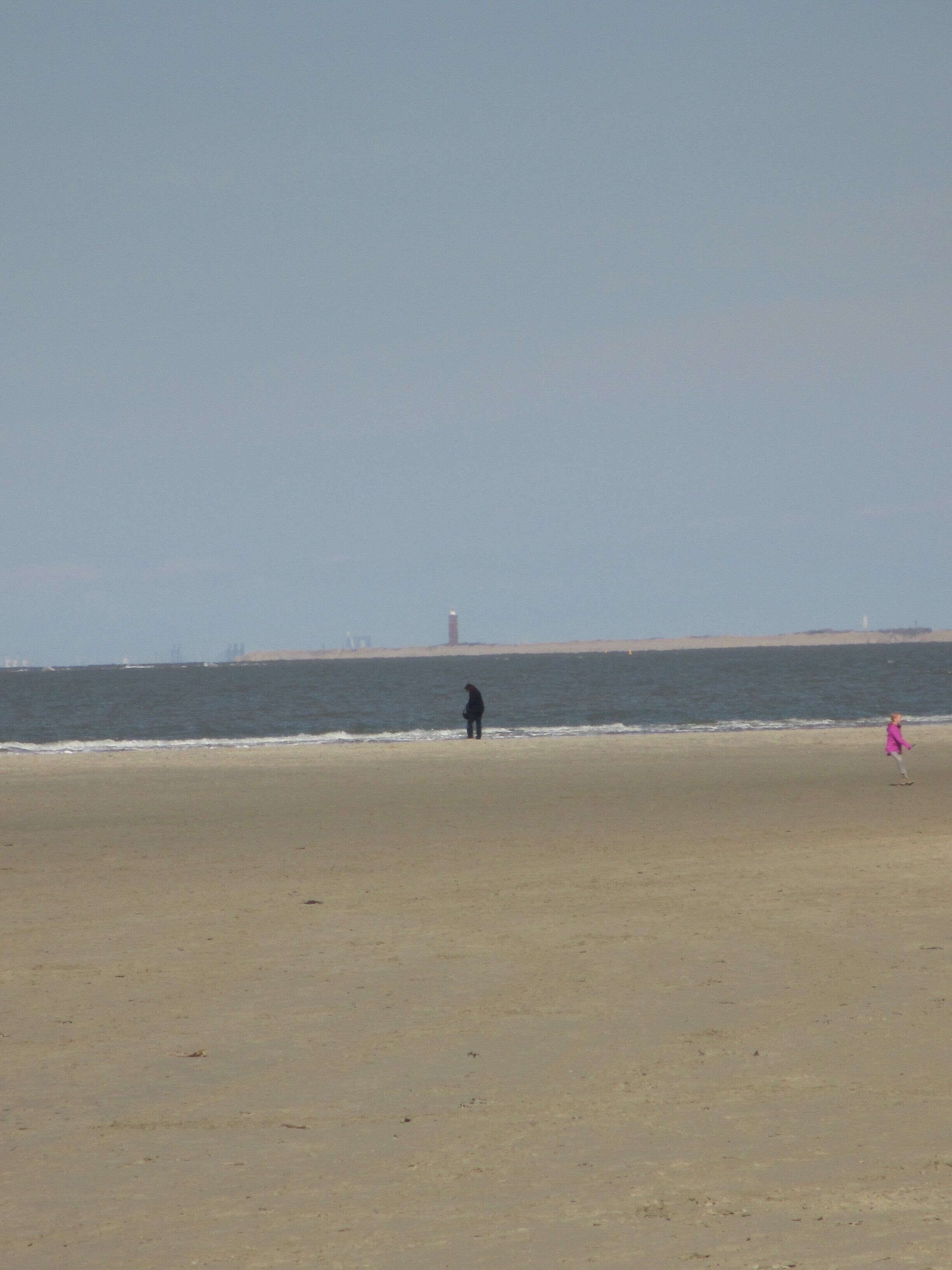 Una playa con una persona de pie cerca de la orilla y otra caminando a lo lejos.