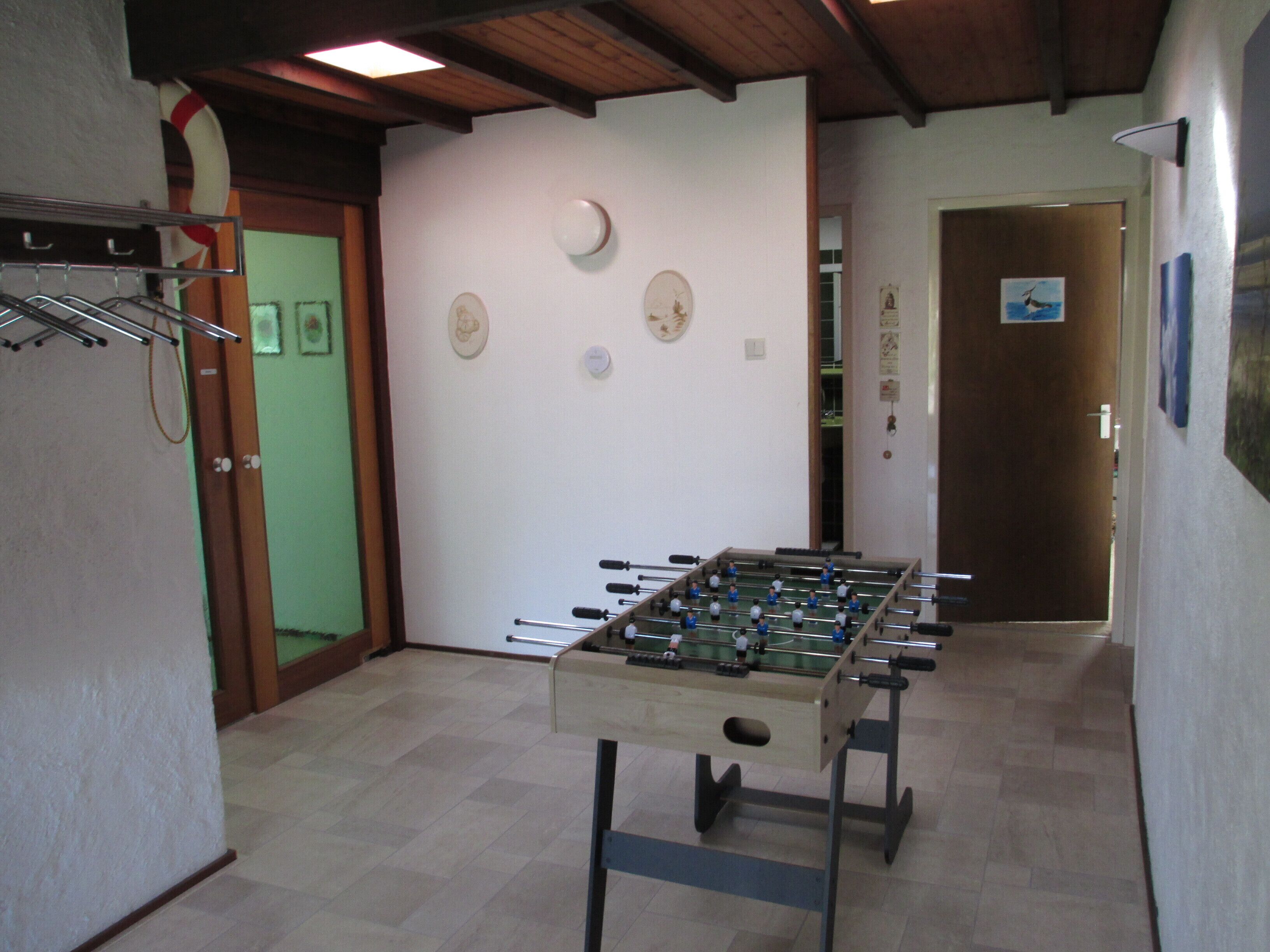 Una habitación con una mesa de fútbol de mesa, una puerta y una pared con un reloj y un cuadro enmarcado.