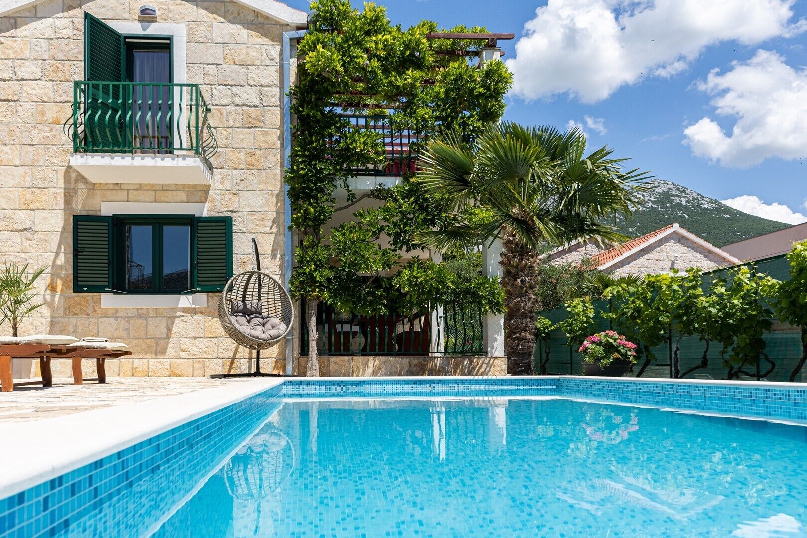 A swimming pool with a stone building and a balcony with green shutters.