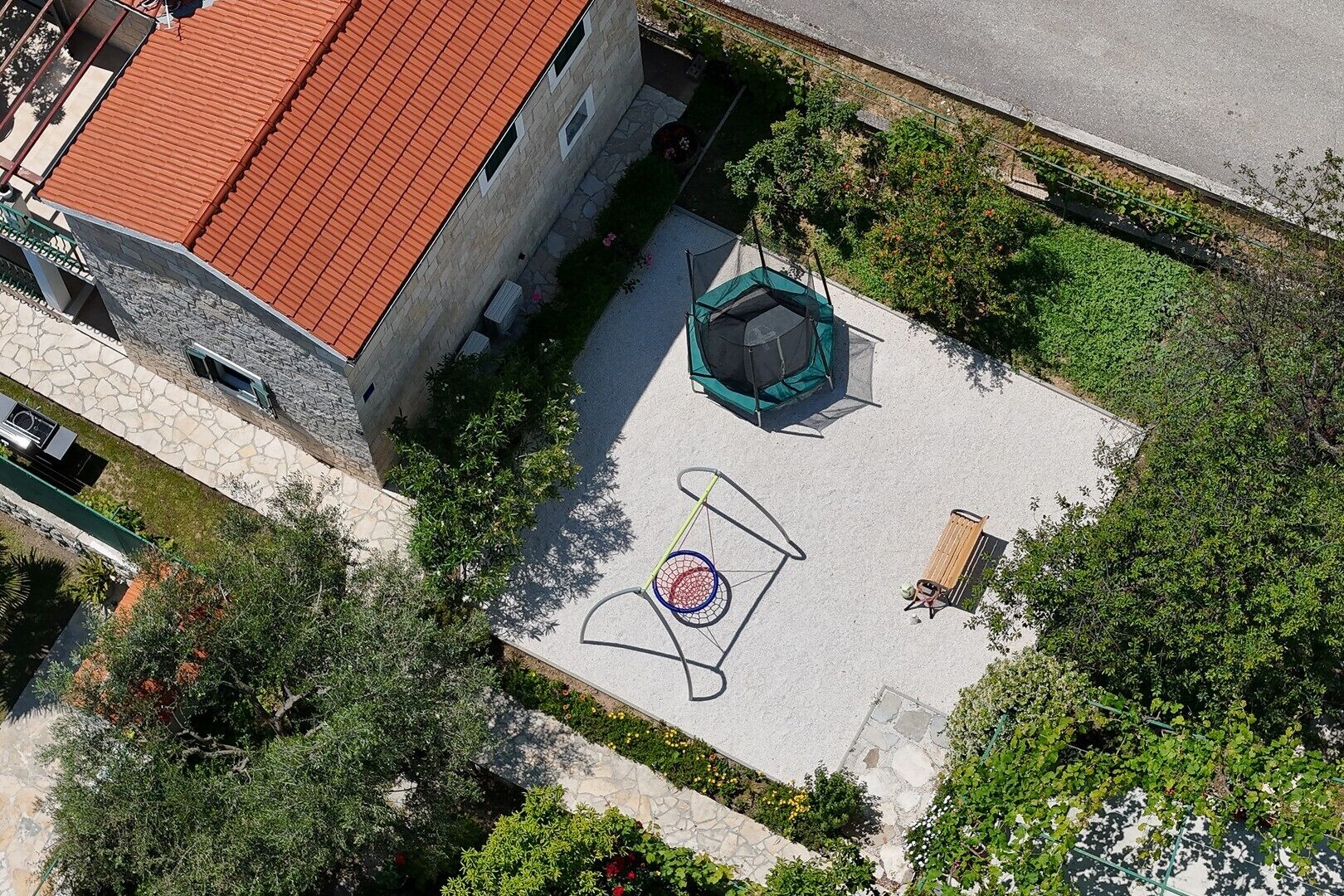 An aerial view of a courtyard with a basketball court, a trampoline, and a stone pathway.