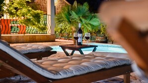 A poolside lounge with two cushioned chairs, a table with a bottle of wine and two glasses, and a stone building in the background. - Villa Josip near Omiš, private pool (Gata)