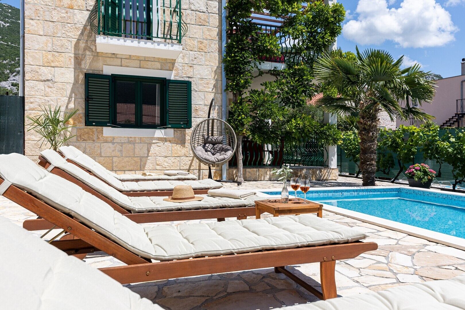 A poolside area with lounge chairs, a wicker chair, and a small table with drinks.