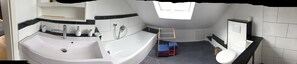 A modern bathroom with a large bathtub, a separate sink, and a toilet. There is a towel rack with folded towels and a small trash bin. - Nice large apartment on the bike path (Harxheim)