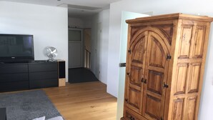 Moderni olohuone, jossa on harmaa sohva, puinen vaatekaappi, televisio ja tuuletin.