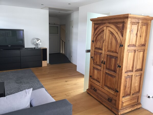 A modern living room with a grey sofa, a wooden wardrobe, a TV, and a fan. - Nice large apartment on the bike path (Harxheim)