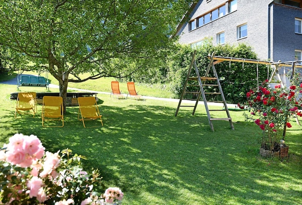 Un espacio al aire libre con césped, un conjunto de columpios, sillas amarillas y una escalera.