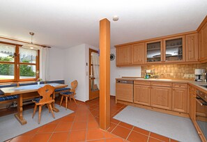 Une cuisine avec des meubles de rangement en bois, une table à manger avec des coussins bleus et une fenêtre avec des rideaux.