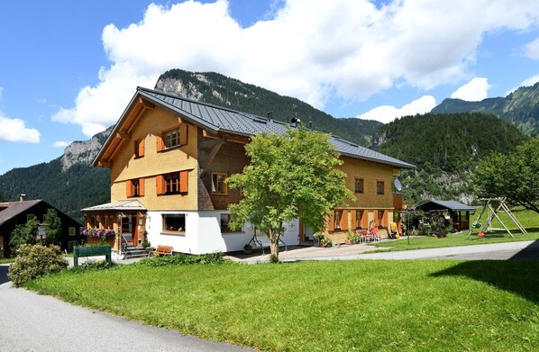 Une maison en bois à deux étages, dotée d’un balcon, entourée d’une pelouse et de montagnes.