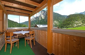 A wooden interior with a table and chairs, large windows, and a view of mountains.
