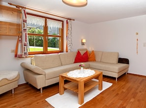 A living room with a sofa, a wooden coffee table with a vase, a window with curtains, and a wall-mounted lamp.