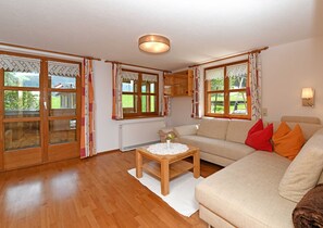 A living room with a sofa, a table, and a view of the outdoors through large windows. - Apartment Fluh - Guesthouse Margreth (Au)