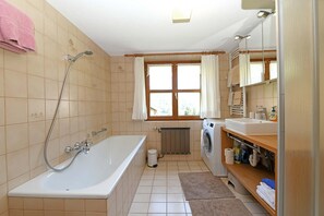 A bathroom with a bathtub, a shower, a window, a washing machine, and a sink.