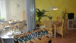 Une pièce avec une table de baby-foot, des meubles en osier, un mur jaune et un téléviseur.