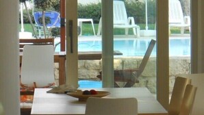 A dining area with a table and chairs, a view of a swimming pool, and outdoor seating with chairs. - Apartment with heated saltwater pool, private garden, air conditioning, WiFi (Donnalucata)