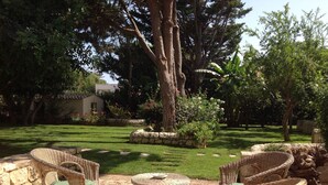 An outdoor seating area with wicker furniture and a stone table, surrounded by a well-maintained lawn and large trees. - Apartment with heated saltwater pool, private garden, air conditioning, WiFi (Donnalucata)